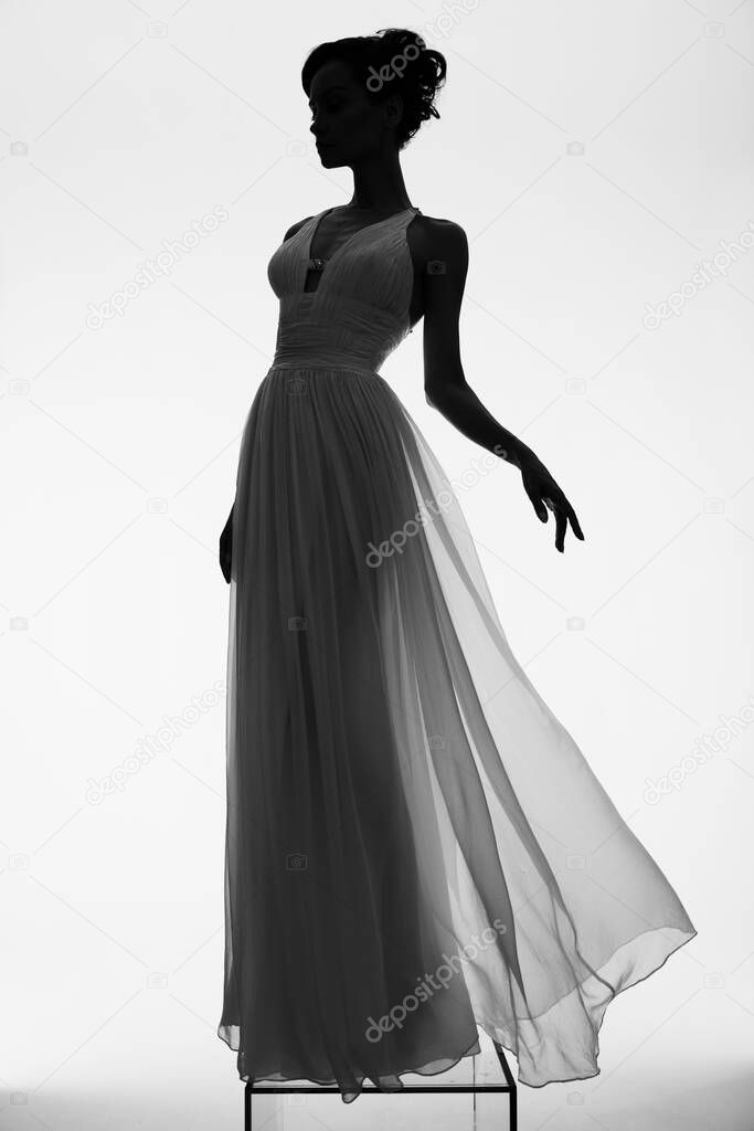 Beautiful young lady posing in a photo studio in a chic dress. Sexy model in bright spotlights. Portrait of a woman in a white wedding dress. Art photography.