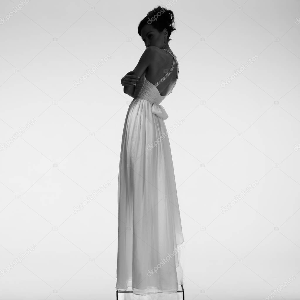Beautiful young lady posing in a photo studio in a chic dress. Sexy model in bright spotlights. Portrait of a woman in a white wedding dress. Art photography.