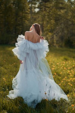 Young beautiful girl in a white wedding dress. Sexy blonde in a chic classic dress posing in nature. Summer sunny day. Beautiful landscape.