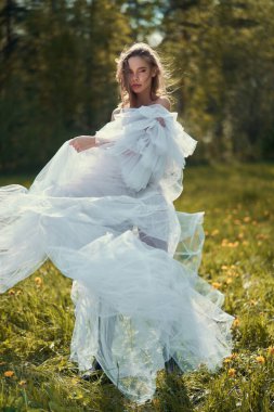 Young beautiful girl in a white wedding dress. Sexy blonde in a chic classic dress posing in nature. Summer sunny day. Beautiful landscape.