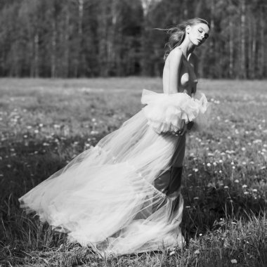 Young beautiful lady in a white wedding dress. Sexy blonde in a chic classic dress posing in nature. Portrait of nude naturist. Summer sunny day. Beautiful landscape.