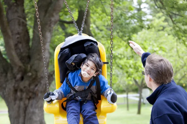 Father pushing disabled son on handicap swing — Stock Photo, Image