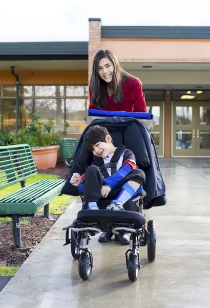 Teenager-Mädchen schubst kleinen behinderten Jungen im Rollstuhl — Stockfoto