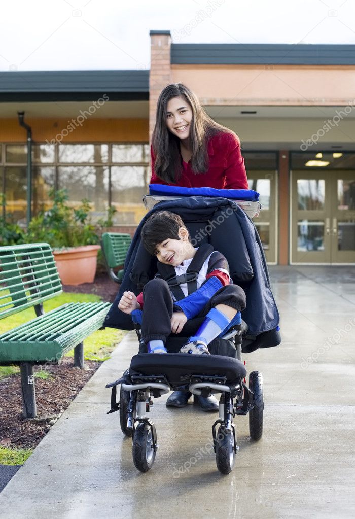 Teenage girl pushing little disabled boy in wheelchair