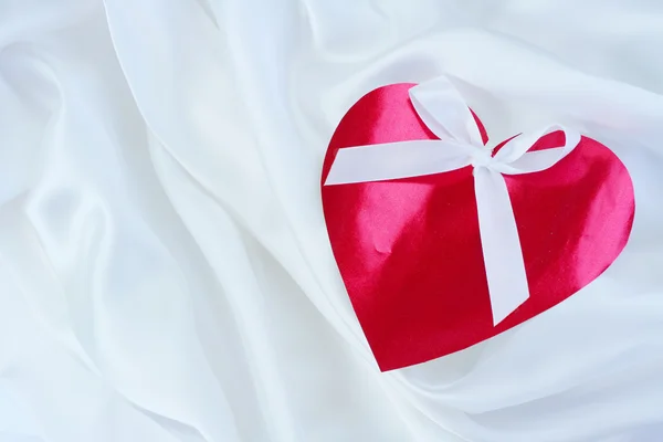 Red heart with ribbon on white satin — Stock Photo, Image