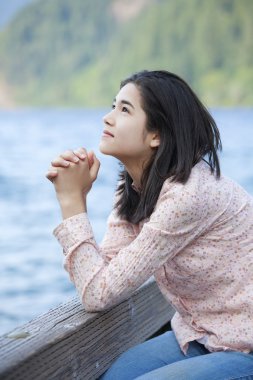 Young teen girl sitting quietly on lake pier, praying clipart