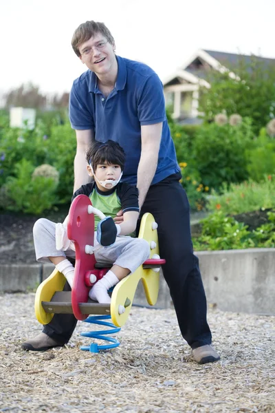 Padre ayudando hijo discapacitado jugar en el patio de recreo —  Fotos de Stock