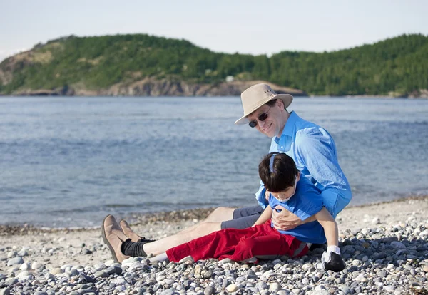 Far sitter på stranden med handikappade son — Stockfoto