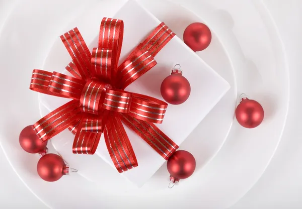 Белый подарок с красными лентами на тарелке — стоковое фото
