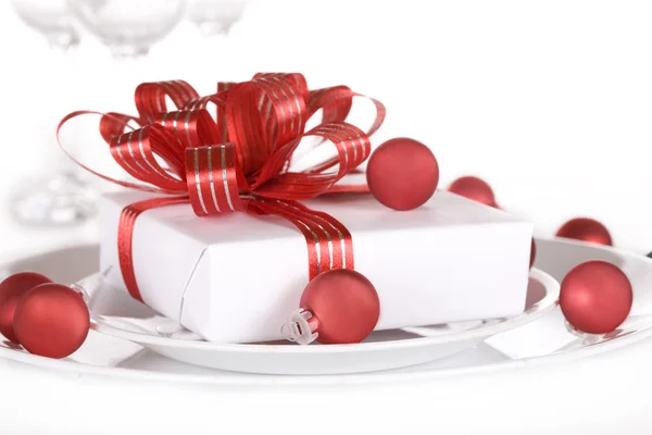 White present with red ribbons on a dinner plate — Stock Photo, Image