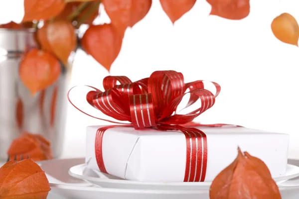 White present with red ribbons on a dinner plate — Stock Photo, Image