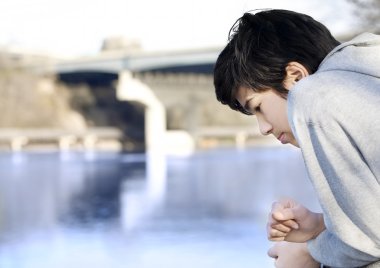 Teen boy sadly looking out over river, thinking clipart
