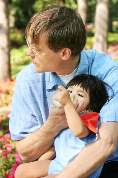 Father feeding baby a bottle in the park — Stock Photo, Image