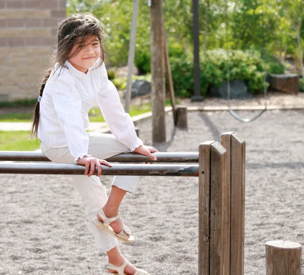 Klein meisje zit op de top van parallelle staven op speelplaats — Stockfoto