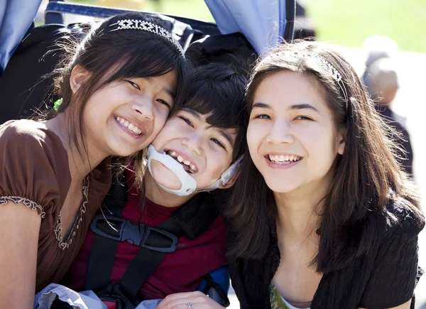 Ragazzo disabile in sedia a rotelle circondato da sorelle maggiori, sorridente — Foto Stock