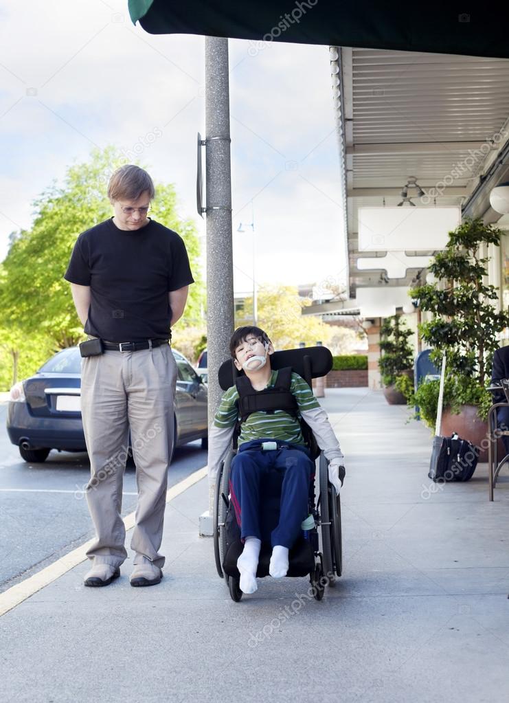 Father walking next to disabled son in wheelchair through town