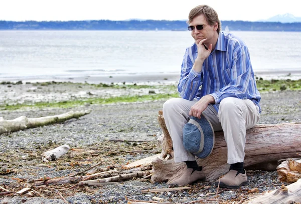 Depressief man zit op drijfhout op strand — Stockfoto