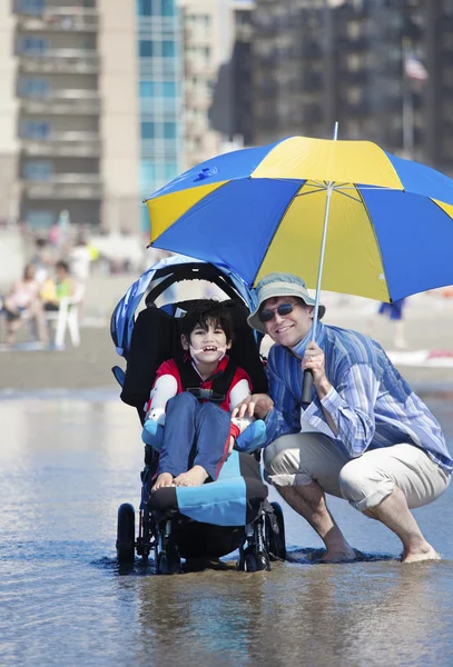 Padre in spiaggia con figlio disabile in sedia a rotelle — Foto Stock