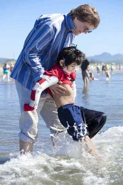 Vater hilft behindertem Sohn am Strand in den Wellen des Ozeans — Stockfoto