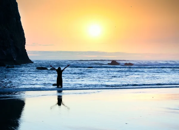 Meisje permanent in golven, armen verhoogd tot de hemel bij zonsondergang — Stockfoto