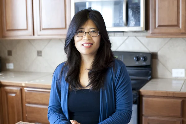 Vacker asiatisk kvinna i tidiga fyrtiotalet stående i köket — Stockfoto