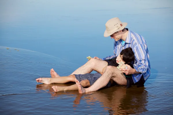 Отец играет с сыном-инвалидом на пляже, держит его прямо — стоковое фото