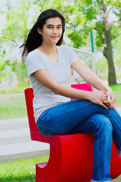 Mooie tiener meisje, zittend buiten op rode stoel — Stockfoto