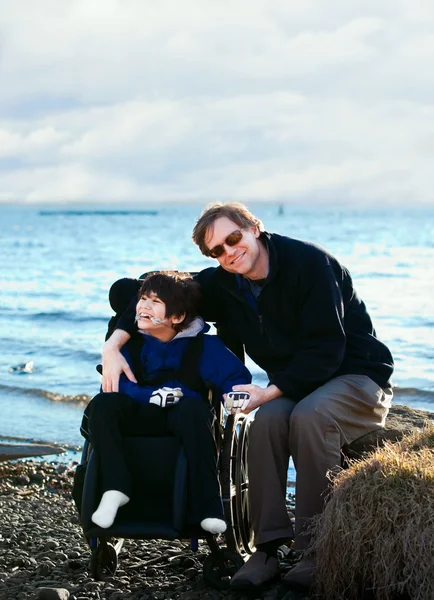 Far sitter med handikappade son längs sjöstranden — Stockfoto