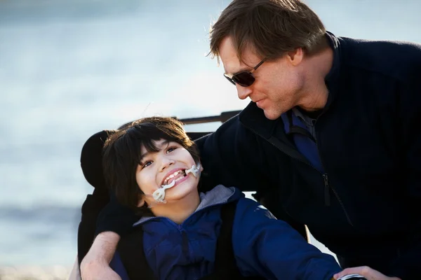 Padre seduto con figlio disabile lungo la riva del lago — Foto Stock