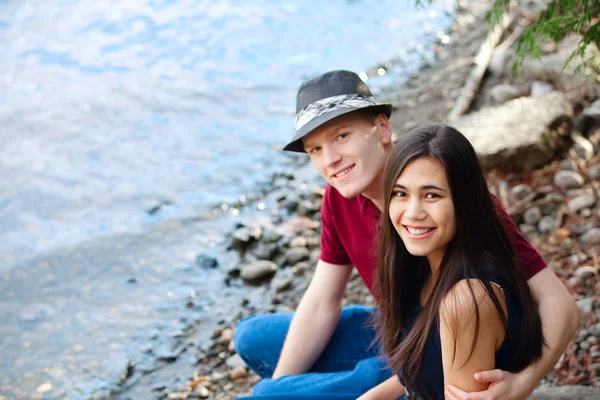 Beau jeune couple interracial assis ensemble au bord du lac shor — Photo