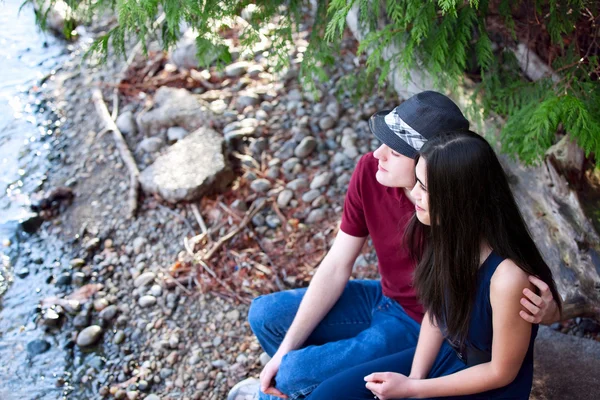 Beautiful young interracial couple sitting together by lake shor — Stock Photo, Image