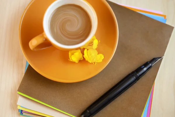Orange coffee cup on brown writing paper with pen — Stock Photo, Image