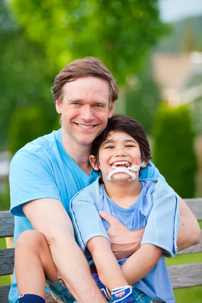 Bonito pai segurando sorrindo filho deficiente ao ar livre — Fotografia de Stock