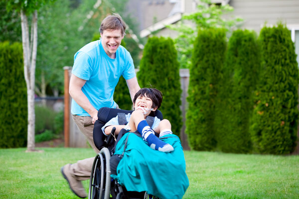 Father racing around park with disabled son in wheelchair