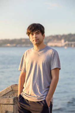 Yakışıklı melez Asyalı, Kafkas melezi genç adam gün batımına yakın gölün kenarında duruyor.