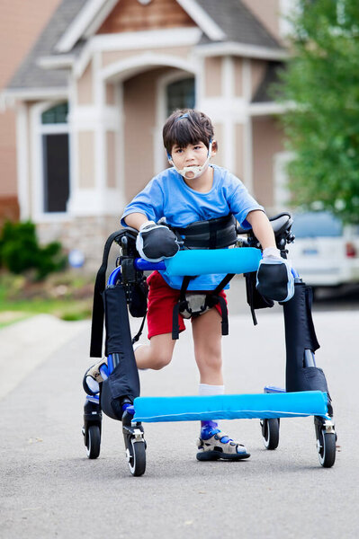 Six year old boy exercising in his gait trainer walker outdoors on road