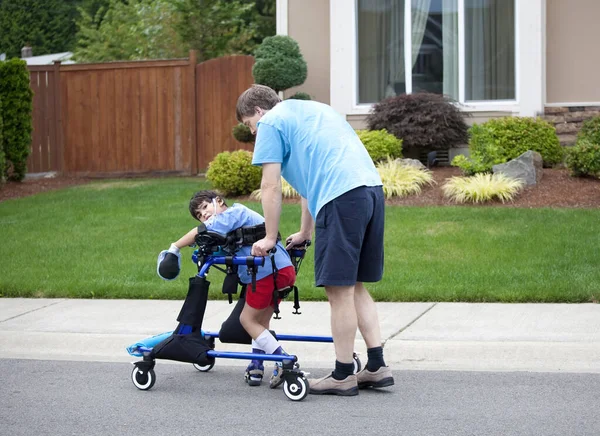 Father Helping Son Walk His Gait Trainer Walker Outdoors Road Stockbild