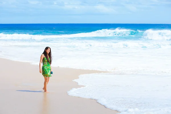 水の端にハワイのビーチに沿って歩く緑のドレスの美しい十代の女の子 ロイヤリティフリーのストック写真