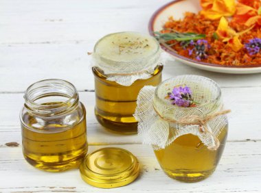 Kavanozda filtreledikten sonra şifalı bitkilerden elde edilen doğal yağ. Ev yapımı şifalı yağ beyaz masadaki cilt için iyidir..