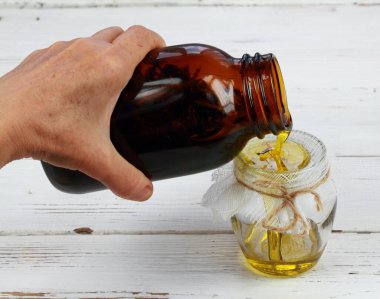 Bitki yağı, şifalı bitkileri filtreleyen kadın. Yağ ve bitkilerle el ele tutuşan şişe. Ev yapımı şifalı yağ cilde iyi gelir..