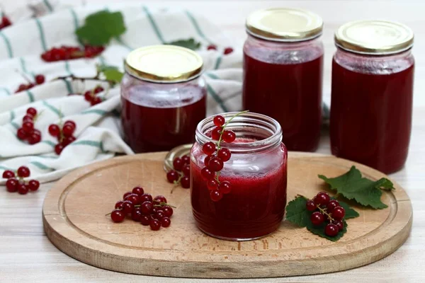 Homemade preserved red currant jam in jars. Red currants and preserved jars on white wooden table.