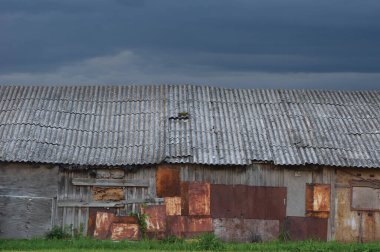 Yaşlı, yıpranmış ahşap kulübe, gri kaplama ahşap kulübe duvarı, yamalı tahtalar, paslı metal plakalar, paslı boya dokusu, bulutlu manzara panoraması, karanlık gökyüzü, bulutlar, grunge zincirli demir çelik çinko yamalar çatının ayrık ayrıntıları, grunge gri kayrak.