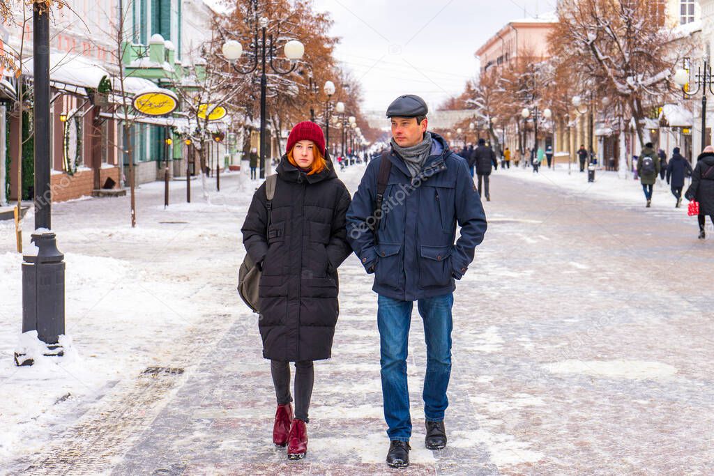 Tourists man and woman walking along city street in winter cloudy day. People spending winter weekend in city. Father and daughter wearing winter casual clothes. Urban vacation concept.