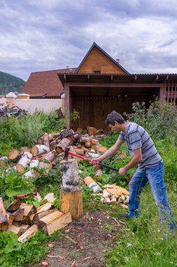 Köy evinin arka bahçesinde baltayla odun kesen orta yaşlı yakışıklı bir adam. Helikopterli bir adam odun yığınının yanında duruyor..
