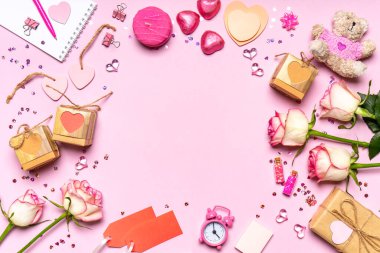 Sevgililer Günün kutlu olsun. Gül çiçeklerinden yapılmış çerçeve, kalpler, hediyeler ve pembe arka planda pembe renkli dekoratif eşyalar. Sevgililer günü için tebrik kartı. Düz konum, üst görünüm, kopyalama alanı.