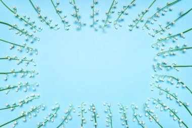 Frame made of fresh white lilies of the valley flowers on blue pastel background. Beautiful natural mock up for greeting card for holiday event. Flat lay, top view, copy space.