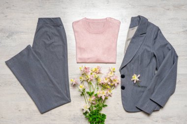 Pembe pastel aksesuarları ve açık arkaplanda buketleri olan gri renkli kadınlar klasiği. Ceket ve pantolon, bluz ve bahar çiçekleri. Güzel şık kıyafetler, şık kıyafetler..