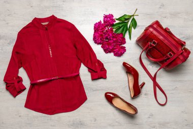 Bluz, el çantası ve kırmızı renkli ayakkabılar. Açık ahşap arka planda taze şakayık çiçekleri. Bahar modasına uygun kıyafetler, günlük tarz kadın kıyafetleri. Moda konsepti.