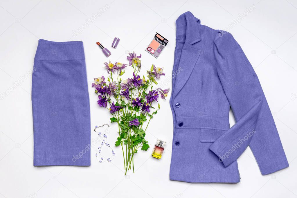 Women classic suit in trendy very peri color of the year 2022. Jacket and skirt on white background. Spring flowers, accessories, cosmetics, perfume. Beautiful stylish clothes, fashionable outfit.