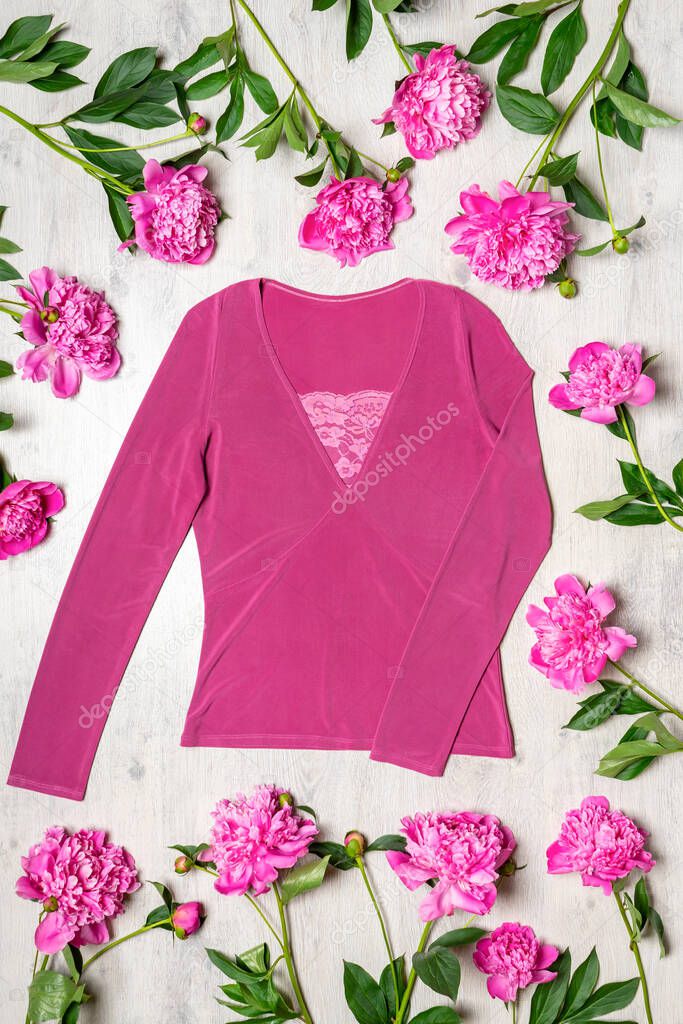 Beautiful clothing blouse in pink colors with fresh peonies flowers on light wooden background. Spring fashionable outfit, casual stylish women's clothes. Fashion concept.